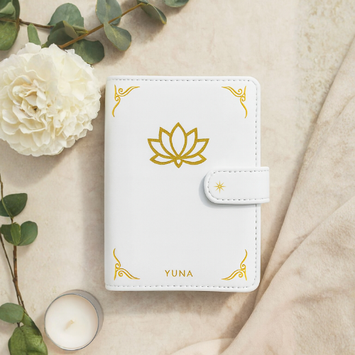 White planner with gold lotus design and 'YUNA' branding on a beige surface with flowers candle.